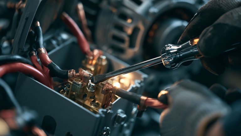 A detailed close-up shot of an off-grid specialist’s gloved hands making final 240V electrical connections using thick, red 6 AWG copper wire inside the junction box of a custom DIY 10kW generator build.